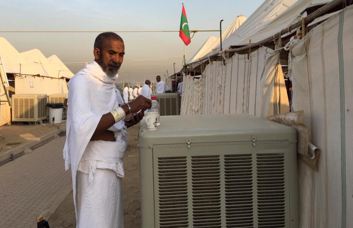 އަރަފާތުގައި ދިވެހިން ތިބި ޓެންޓުތަކަށް ފިނި ވައި ފޮނުވަން ބަހައްޓާފައި ހުންނަ އެއާ ކޫލަރެއްގެ ކައިރީގައި ދިވެހި ހައްޖުވެރިއަކު ހުއްޓިލައިގެން. ފޮޓޯ ހައްޖު ކޯޕަރޭޝަން