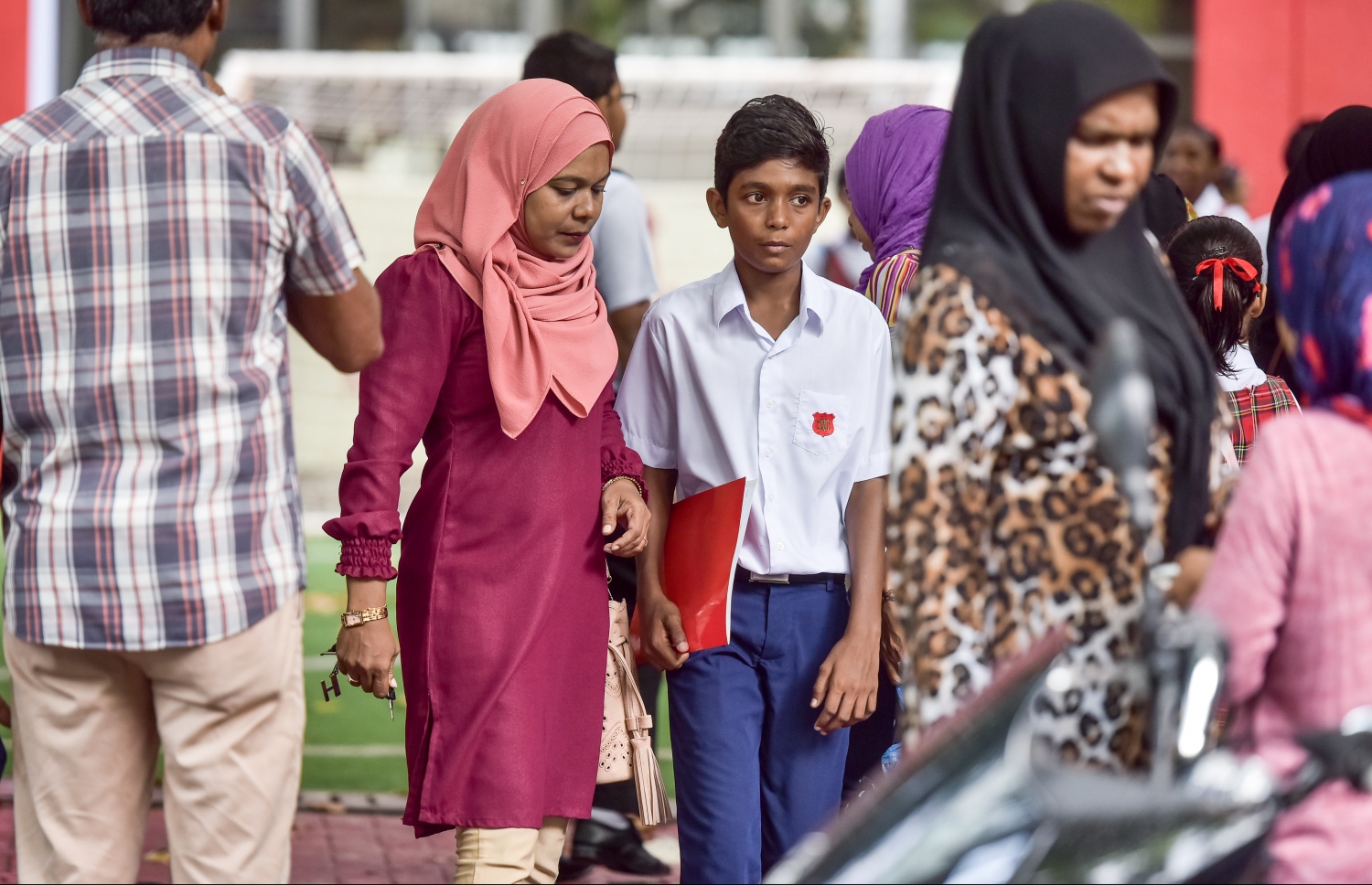 މަޖީދިއްޔާ ސްކޫލުގެ ދަރިވަރަކު، އޭނާގެ ބެލެނިވެރިއާއެކު ރިޕޯޓު ފޮތް ހިފައިގެން ދަނީ.-- ފޮޓޯ: ނިޝާން އަލީ/ މިހާރު