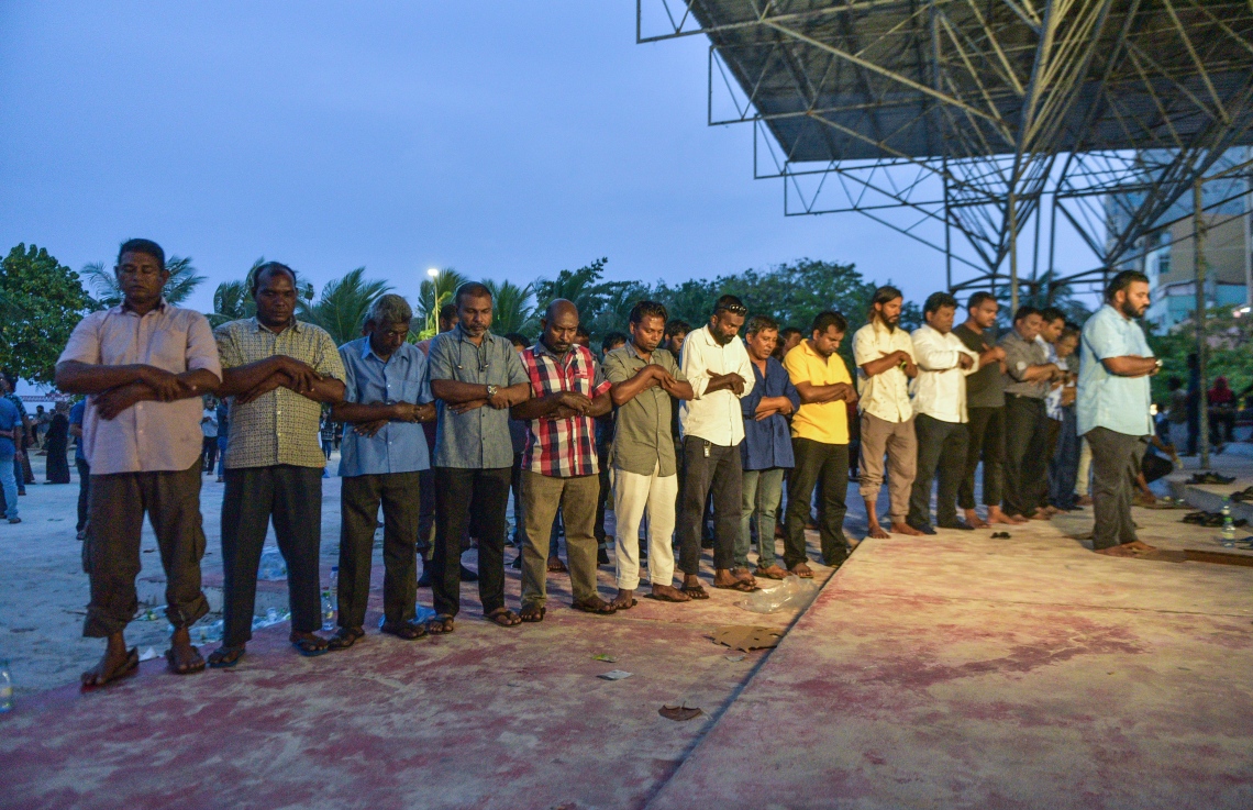 މާލެ: ފެބްރުއަރީ 16، 2018- ސަރުކާރާ ދެކޮޅަށް އިދިކޮޅު ހަރަކާތުން ފަހުގެ ތާރީޚެއްގައި ބާއްވާ ބޮޑު މުޒާހަރާ އަށް ތައްޔާރުވުމަށް "ވޯމްއަޕް މުޒާހަރާ" ގެ ނަމުގައި އެމްޑީޕީގެ ހަރުގެ ކައިރީގައި ކުރިއަށް ގެންދަން އުޅުނު އެއްވުން ފުލުހުން ރޫޅާލުމަށް ފަހު، އެއްވުމުގެ ބައެއް ބައިވެރިން އާޓިފިޝަލް ބީޗް ސަރަހައްދުގައި މަޣްރިބު ނަމާދު ކުރަނީ.---ފޮޓޯ: ހުސެއިން ވަހީދު/މިހާރު