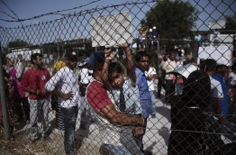A man carries a young boy behind a fence during a visit of the UN secretary-general at the refugee camp of Kara Tepe in Mytilene on June 18, 2016. UN Secretary General Ban Ki-moon headed on June 18 to take a first-hand look in Greece at the migration crisis that has engulfed Europe, as tens of thousands of migrants remain blocked at the doorstep to the EU. / AFP PHOTO / ANGELOS TZORTZINIS