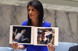 US Ambassador to the UN, Nikki Haley holds photos of victims as she speaks as the UN Security Council meets in an emergency session at the UN on April 5, 2017, about the suspected deadly chemical attack that killed civilians, including children, in Syria. / AFP PHOTO / TIMOTHY A. CLARY