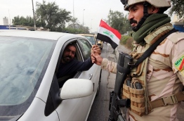 An Iraqi man gives a soldier a national flag at a checkpoint in the capital Baghdad on January 6, 2018, during festivities marking Iraq's Army Day. / AFP PHOTO / SABAH ARAR