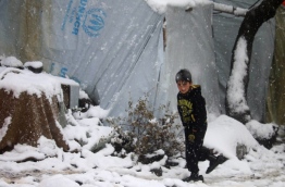 A displaced Syrian child walks through a blizzard at a make-shift refugee camp near the village of Burayqah on the outskirts of southeastern Syrian border town of Quneitra, on January 26, 2018. / AFP PHOTO / Mohamad ABAZEED