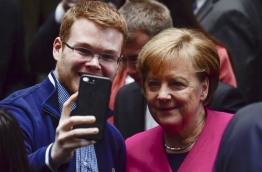 German Chancellor Angela Merkel poses for a selfie with an unidentfied wellwisher on March 12, 2018 in the Bundestag compound in Berlin, after the signature of the chancellor's conservative CDU/CSU and the SPD's coalition contract for a new government. / AFP PHOTO / John MACDOUGALL
