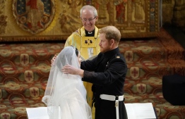 Britain's Prince Harry, Duke of Sussex (R) removes the veil of US actress Meghan Markle (L) as they stand at the altar together before Archbishop of Canterbury Justin Welby (C) in St George's Chapel, Windsor Castle, in Windsor, on May 19, 2018 during their wedding ceremony. / AFP PHOTO / POOL / Owen Humphreys
