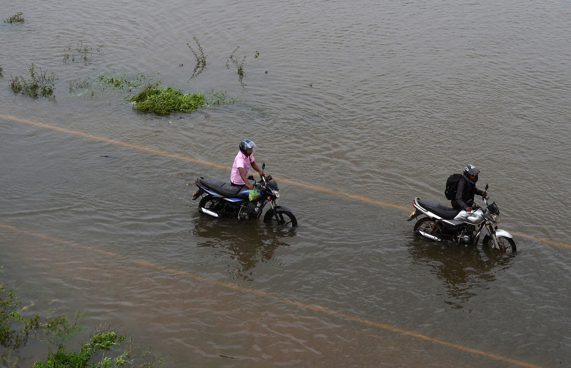 ވެރިރަށް ކޮލަމްބޯގެ ކަޑުވެލައިގައި ފެންބޮޑުވެފައިވާ ސަރަހައްދަކުން ބަޔަކު މޮޓޯސައިކަލް ކޮއްޕައިފައި ގެންދަނީ. --ފޮޓޯ:އޭއެފްޕީ