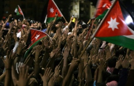 Protesters raise their hands and wave flags near members of the gendarmerie and security forces during a demonstration outside the prime minister's office in the capital Amman late on June 3, 2018.
Jordan's senate met on June 3 for a special session after another night of protests across the country against IMF-backed austerity measures including a draft income tax law and price hikes. Some 3,000 people faced down a heavy security presence to gather near the prime minister's office in Amman until the early hours of Sunday morning. / AFP PHOTO / Khalil MAZRAAWI