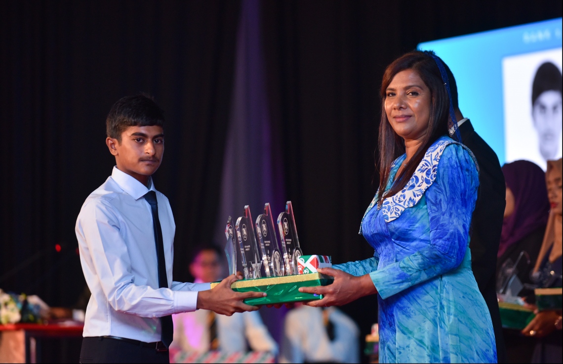 މާލެ: ޖުލައި 9، 2018- މިދިޔަ އަހަރުގެ އޮކްޓޯބަރު/ނޮވެމްބަރުގައި ބޭއްވި އޭ ލެވެލް އިމްތިހާނުގެ ރަންވަނަތައް ހޯދި ދަރިވަރުންނަށް އިނާމު ދިނުމަށް ދަރުބާރުގޭގައި ބޭއްވި ރަސްމިއްޔާތުގައި، އެޑިއުކޭޝަން މިނިސްޓަރު އާއިޝަތު ޝިހާމް، ދަރިވަރަކަށް އެވޯޑާއި އިނާމު ދެއްވަނީ.---ފޮޓޯ: ހުސެއިން ވަހީދު/މިހާރު