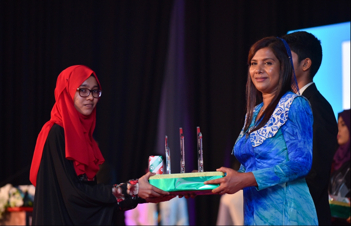 މާލެ: ޖުލައި 9، 2018- މިދިޔަ އަހަރުގެ އޮކްޓޯބަރު/ނޮވެމްބަރުގައި ބޭއްވި އޭ ލެވެލް އިމްތިހާނުގެ ރަންވަނަތައް ހޯދި ދަރިވަރުންނަށް އިނާމު ދިނުމަށް ދަރުބާރުގޭގައި ބޭއްވި ރަސްމިއްޔާތުގައި، އެޑިއުކޭޝަން މިނިސްޓަރު އާއިޝަތު ޝިހާމް، ދަރިވަރަކަށް އެވޯޑާއި އިނާމު ދެއްވަނީ.---ފޮޓޯ: ހުސެއިން ވަހީދު/މިހާރު