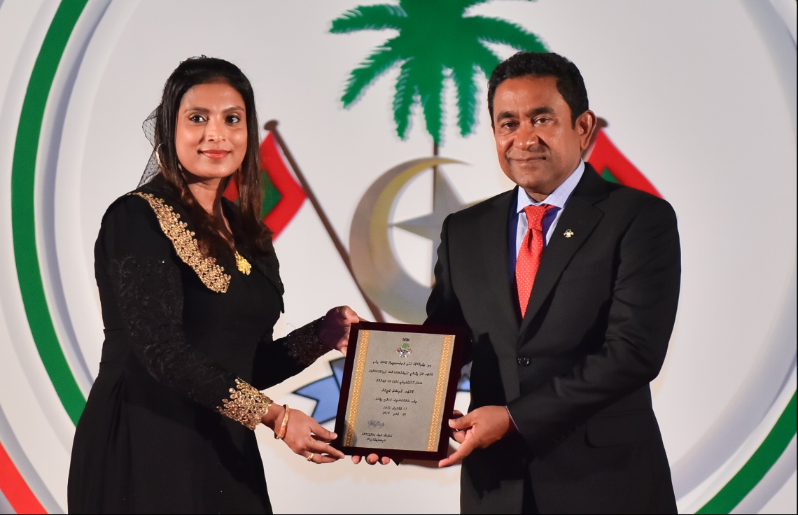 މާލެ: ޖުލައި 26، 2018- ރާއްޖޭގެ މިނިވަން ކަމަށް 53 އަހަރު ފުރުން ފާހަގަ ކުރުމަށް ޖުމްހޫރީ މައިދާނުގައި ބޭއްވި ރަސްމިއްޔާތުގައި، ދިވެހި ގައުމީ ޔުނިވަސިޓީން ފުރަތަމަ ޕީއެޗްޑީ ހެއްދެވި ދެ ބޭފުޅުންގެ ތެރެއިން ޑރ. އާއިޝަތު އަލީ އަށް ރައީސް ޔާމީން، ހަނދާނީ ފިލާ ދެއްވަނީ.---ފޮޓޯ: ހުސައިން ވަހީދު/މިހާރު