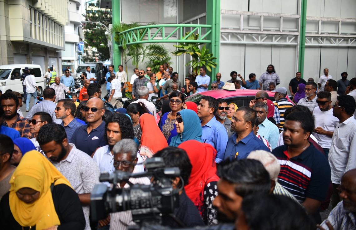 މާލެ: އޮގަސްޓް 10، 2018- އިދިކޮޅު ކޯލިޝަނުން ބޭއްވި މުޒާހަރާއެއްގައި ދެއްކި ވާހަކަތަކެއް ބްރޯޑްކާސްޓް ކުރުމުން ދެ މިލިއަން ރުފިޔާއިން ޖޫރިމަނާ ކޮށްފައިވާ ރާއްޖެ ޓީވީ އަށް އެ ފައިސާ ހޯދައިދޭން "އަބުރުފުޅު ފަންޑު" ގެ ނަމުގައި ފޮއްޓެއް ހުޅުވުމަށް، އެ ސްޓޭޝަން ހިންގާ އިމާރާތުގެ ކުރިމަތީގައި ބޭއްވި ރަސްމިއްޔާތަށް ދިޔަ ބައެއް މީހުން.---ފޮޓޯ: އަހުމަދު ނިޝާތު/މިހާރު