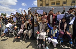 Injured Yemeni Huthi rebel fighters in seated wheelchairs and standing chant slogans during a demonstration demanding the right for the injured to travel abroad for medical treatment, outside the UN offices in the capital Sanaa on September 12, 2018. / AFP PHOTO
