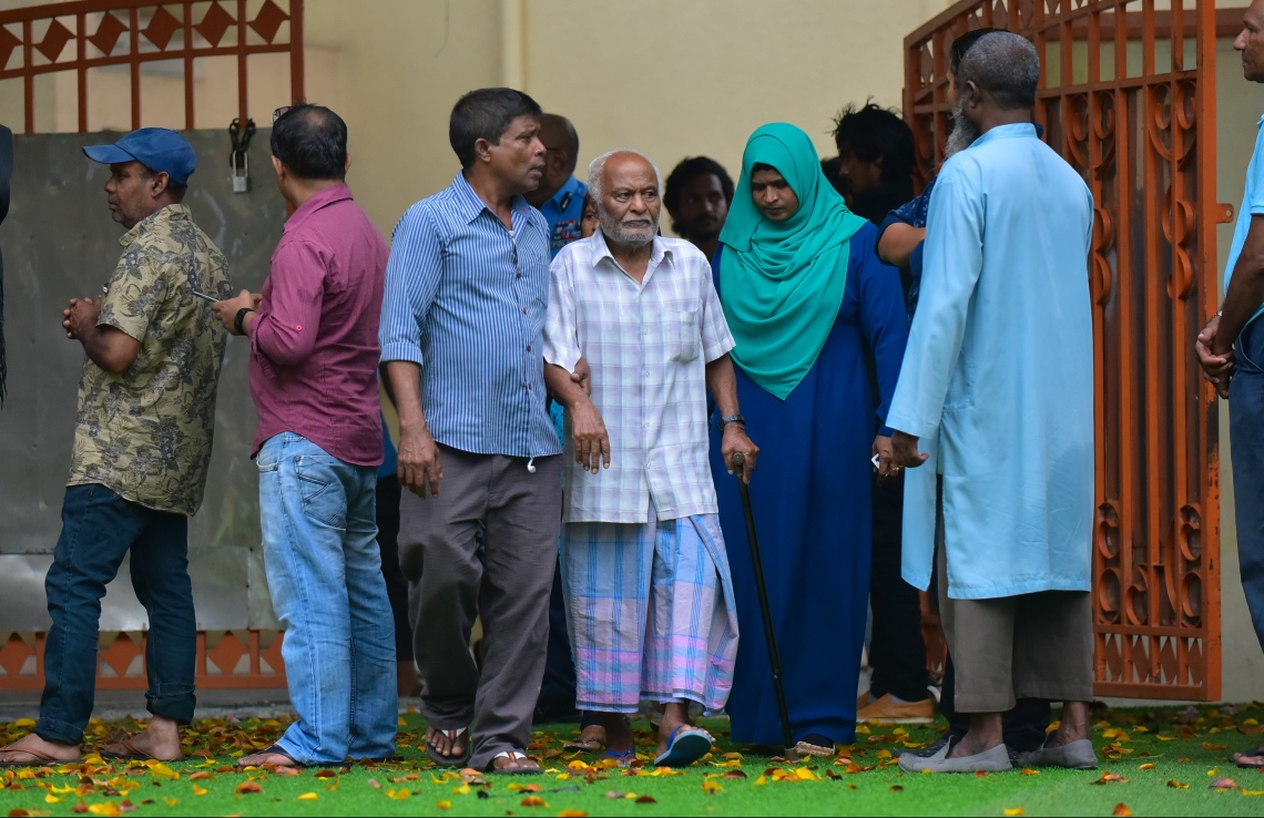 މާލެ: ސެޕްޓެމްބަރު 23، 2018: ރިޔާސީ އިންތިހާބުގެ ވޯޓުލުން: އިމާދުއްދީން ސުކޫލުގައި ބަހައްޓާފައިހުރި ވޯޓު ފޮއްޓަކަށް ވޯޓުލާންދާ އުމުރުން ދުވަސްވީ މީހަކު ދެމީހެއްގެ އެހީއާއެކު ސުކޫލު ހޯލަށް ވަންނަނީ.--ފޮޓޯ: ހުސައިން ވަހީދު/މިހާރު