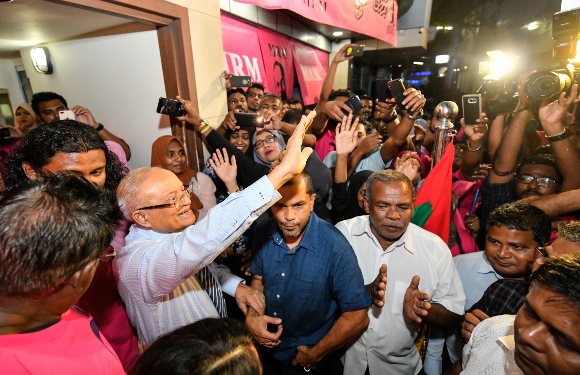 މާލެ: ސެޕްޓެމްބަރު 30، 2018- ގާނޫނާ ޚިލާފަށް ވެރިކަން ވައްޓާލަން އުޅުނު ކަމުގެ ތުހުމަތުގައި ހައްޔަރުކުރުމަށްފަހު މާފުށީ ޖަލުގައި ހުކުމް ތަންފީޒު ކުރައްވަމުން ގެންދެވި ކުރީގެ ރައީސް މައުމޫން އަބްދުލްގައްޔޫމް ކަފާލާތުގެ ދަށުން މިނިވަންވެ ވަޑައިގަތުމަށްފަހު އެންދެރިމާގެއަށް ވަޑައިގަތުމަށްފަހު އެމަނިކުފާނަށް މަރުހަބާ ދެންނެވުމަށް އެސަރަހައްދަށް އެއްވެ ތިބި މީހުންނަށް އަތުން އިޝާރާތްކުރައްވާ ސަލާމްކުރައްވަނީ---ފޮޓޯ: ހުސައިން ވަހީދު/މިހާރު