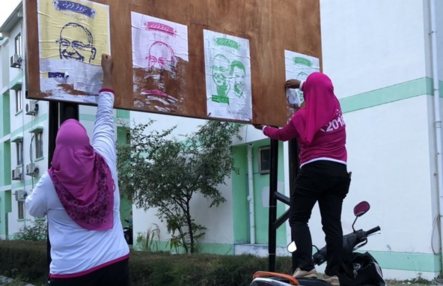 ރައީސް ޔާމީންގެ ފޮޓޯފުޅު ހަރުކުރަން އެޗްޑީސީން ހެދި ބޯޑެއްގައި، އިދިކޮޅު ކެންޑިޑޭޓާއި ރަނިން މޭޓުގެ ޕޯސްޓަރެއް ހަރުކުރުމުން އެޗްޑީސީގެ ދެ މުވައްޒަފަކު އެ ޕޯސްޓަރު ނައްޓާލަނީ. --ފޮޓޯ/ސޯޝަލްމީޑިއާ