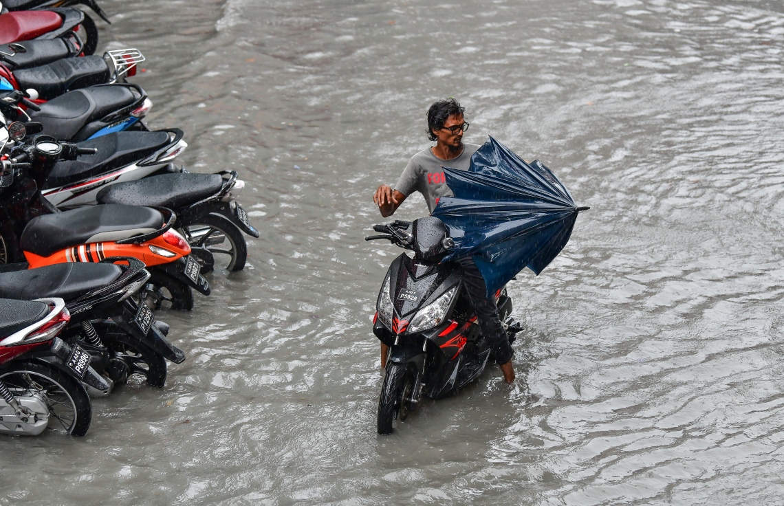 މާލެ: އޮކްޓޯބަރު 28، 2018- މާލެ އަށް މިއަދު ހެނދުނުއްސުރެ ފެށިގެން ވެހެމުންދާ ބޯ ވާރެއާ ގުޅިގެން ފެން ބޮޑުވެފައިވާ މަގަކުން ސައިކަލްގައި ދަމުން މީހަކު ކުޑަ ނަގަނީ: މާލޭގެ ބައެއް މަގުތަކުގައި މިއަދު ވަނީ އާދަޔާ ޚިލާފަށް ފެން ބޮޑުވެ، ހިނގައިބިނގައި އުޅުމަށް ބޮޑެތި ދަތިތަކެއް ކުރިމަތިވެފައި.---ފޮޓޯ: ނިޝާން އަލީ/މިހާރު