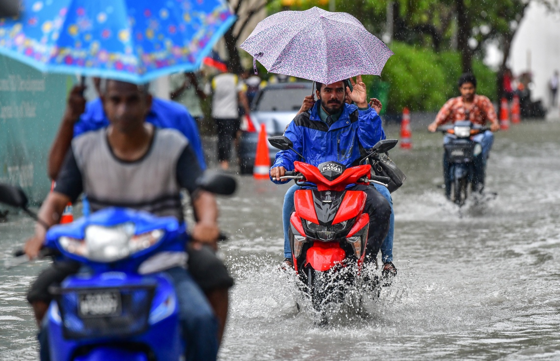 މާލެ: އޮކްޓޯބަރު 28، 2018- މާލެ އަށް މިއަދު ހެނދުނުއްސުރެ ފެށިގެން ވެހެމުންދާ ބޯ ވާރޭގެ ތެރޭގައި ކުޑަ އަޅައިގެން ބަޔަކު، ފެން ބޮޑުވެފައުވާ މަގެއްގައި ސައިކަލްގައި ދަނީ: މާލޭގެ ބައެއް މަގުތަކުގައި މިއަދު ވަނީ އާދަޔާ ޚިލާފަށް ފެން ބޮޑުވެ، ހިނގައިބިނގައި އުޅުމަށް ބޮޑެތި ދަތިތަކެއް ކުރިމަތިވެފައި.---ފޮޓޯ: ނިޝާން އަލީ/މިހާރު