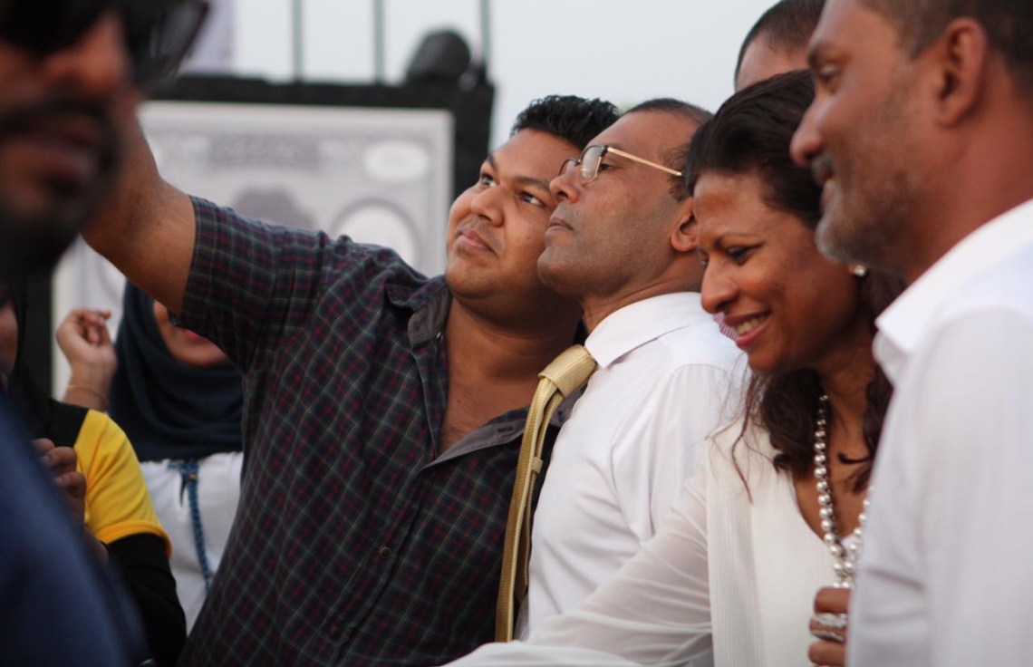 އައްޑޫ :ނޮވެމްބަރު 5، 2018: ކުރީގެ ރައީސް މުހައްމަދު ނަޝީދު އައްޑޫއަށް ކުރެއްވި ދަތުރުފުޅުގައި ނަޝީދަށް މަރުހަބާ ކިއުމަށް އެއްވެ ތިބި މީހުންގެ ތެރެއިން މީހަކާ އެމަނިކުފާނާއެކު ސެލްފީއެއް ނަގަނީ.-- ފޮޓޯ: އެމްޑީޕީ