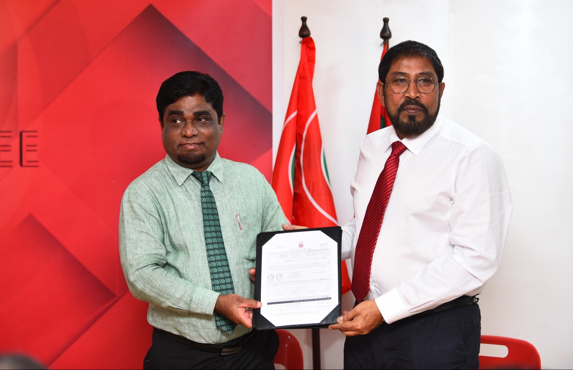 މާލެ: ނޮވެމްބަރު 25، 2018- ދީނީ އިލްމުވެރިޔާ ޑރ. ގުބާދު އަބޫބަކުރު ޖުމްހޫރީ ޕާޓީއަށް ސޮއިކުރެއްވުމަށް ފަހު އޭނާގެ ފޯމު އެ ޕާޓީގެ ލީޑަރު ގާސިމް އިބްރާހީމްއާ ހަވާލު ކުރައްވަނީ.---ފޮޓޯ: ހުސައިން ވަހީދު/މިހާރު