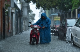 A civilian dragging their motorcycle on a flooded road in Male' City during a downpour.