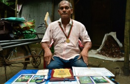 In this photograph taken on October 13, 2018, Bangladeshi tree environmentalist Ohid Sarder, 53, poses with medal, crests, and certificates received for his tree-saving work in Jessore, a western district of Bangladesh. - The 53-year-old self-professed tree hugger has been riding his bicycle across the country, in a grassroots effort to free trees of the billboards and clutter nailed to their trunks. Trees are rampantly misused in Bangladesh as free advertising space, with every available inch of wood plastered with placards until the trunk is barely visible. (Photo by REDWAN AHMED / AFP) / 