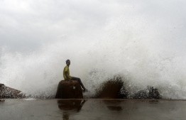 An Indian youth sits on a concrete block as waves hit a breakwater at Kasimedu fishing harbour as cyclone Phethai approaches the eastern Indian coast, in Chennai on December 16, 2018. - Cyclone Phethai is expected to make a landfall on December 17 with winds with a speed of 45-55 kmph, local media reported. (Photo by ARUN SANKAR / AFP)