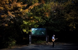 In this picture taken on November 1, 2018 Japanese musician Kyochi Watanabe plays his guitar as he poses for a photo at the entrance of Aokigahara Forest, known as Suicide Forest, in Narusawa village, Yamanashi prefecture. - Japanese musician Kyochi Watanabe has waged an eight-year battle to try to turn back people who come to what is known as Japan's "Suicide Forest" -- using music to try to snap people out of their anguish. In the 1970s it being increasingly depicted in popular novels, movies and television dramas as the fictional setting for suicides and the association eventually became strong enough that suicidal people began travelling to the forest to die, often hanging themselves from its towering trees. (Photo by Behrouz MEHRI / AFP) / 