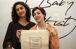 Palestinian fashion designer and label founder Yasmeen Mjalli (L), along with her creative director Amira Khader, pose for a picture with one of their label "BabyFist's" canvas bags in their shop in Ramallah in the occupied West Bank on December 19, 2018. - It's only three words on a T-shirt or embroidered on a denim jacket, but they carry a powerful message: "Not you habibti (darling)." "BabyFist" label founder Yasmeen Mjalli, 22, sees the clothes helping to empower Palestinian women facing unwelcome male attention in public, placing on the fabrics of muted colours and on canvas bags messages in English and Arabic inside drawings of flowers and other designs. (Photo by ABBAS MOMANI / AFP)