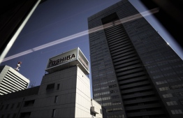Toshiba Corp. signage displayed atop the company's headquarters is seen through a train window in Tokyo, Japan, on Monday, Jan. 23, 2017. Toshiba's shares climbed the most in three weeks on Monday after reports that the company’s plan to sell a stake in its chip unit is drawing attention from possible investors. Photographer: Kiyoshi Ota/Bloomberg