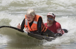 Pamela Hanford, 75, is helped by a team of coaches and volunteers to surf at an adaptive surfing event at Muizenberg beach, on January 20, 2019, in Cape Town, South Africa. - Hansford broke her neck while bodyboarding, but was determined to get back into the sea, even though she can't walk. Adaptive surfing is an initiative aimed at giving disabled people access to the ocean, and to surfing in particular. This is made possible by having a team of coaches and helpers to get the surfers in and out of the water, safely. (Photo by RODGER BOSCH / AFP)