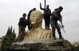 Fighters atop a torn down statue of former Syrian president Hafiz Al Assad. PHOTO: Cable News Network (CNN)