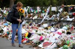 A woman walks past flowers and tributes displayed in memory of the twin mosque massacre victims at the Botanical Garden in Christchurch on March 29, 2019. - The remembrance ceremony is being held in memory of the 50 lives that were lost in the March 15th mosque shootings in Christchurch. (Photo by Sanka VIDANAGAMA / AFP)