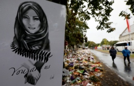 People walk past flowers and tributes displayed in memory of the twin mosque massacre victims outside the Botanical Gardens in Christchurch on April 5, 2019. - The man accused of shooting dead 50 Muslim worshippers in a Christchurch mosque sat impassively April 5 as a New Zealand judge ordered him to undergo tests to determine if he is mentally fit to stand trial for murder. (Photo by Sanka VIDANAGAMA / AFP)
