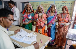 An official checks the names of Indian lambadi tribeswomen at a polling station during India's general election at Pedda Shapur village on the outskirts of Hyderabad on April 11, 2019. - India's mammoth six-week general election kicked off April 11, with polling stations in the country's northeast among the first to open. (Photo by NOAH SEELAM / AFP)