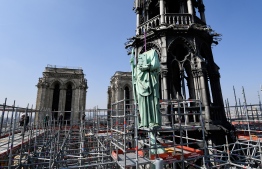 One of 16 copper statues, sitting 50 meters above the ground, is lifted off the Notre-Dame-de-Paris Cathedral to be taken for restoration on April 11, 2019 in the French capital Paris. - Using a 120 meter crane at the foot of the cathedral, the sixteen statues, the 12 apostles and the 4 evangelists, which sit around the spire of the cathedral are being removed to be sent to Perigueux, in southwest France for restoration. The absence of the statues will also signal the start of the renovation work of the spire that will last until 2022. Only then will the statues,  commisioned in the 1860s during the great restoration of the cathedral by Viollet-le-Duc, return to their original place. (Photo by BERTRAND GUAY / AFP)