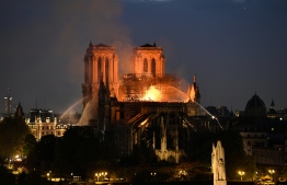 Firefighters douse flames rising from the roof at Notre-Dame Cathedral in Paris on April 15, 2019. - A major fire broke out at the landmark Notre-Dame Cathedral in central Paris sending flames and huge clouds of grey smoke billowing into the sky, the fire service said. The flames and smoke plumed from the spire and roof of the gothic cathedral, visited by millions of people a year, where renovations are currently underway. (Photo by Bertrand GUAY / AFP)