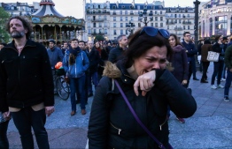 A woman cries as people look at Notre-Dame de Paris Cathedral engulfed in flames from the Paris's Hotel de Ville esplanade on April 15, 2019. - A huge fire swept through the roof of the famed Notre-Dame Cathedral in central Paris on April 15, 2019, sending flames and huge clouds of grey smoke billowing into the sky. The flames and smoke plumed from the spire and roof of the gothic cathedral, visited by millions of people a year. (Photo by STR / AFP)