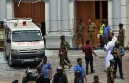 An ambulance is seen outside the church premises with gathered people and security personnel following a blast at the St. Anthony's Shrine in Kochchikade, Colombo on April 21, 2019. - At least 42 people were killed April 21 in a string of blasts at hotels and churches as worshippers attended Easter services, a police official told AFP. (Photo by ISHARA S. KODIKARA / AFP)