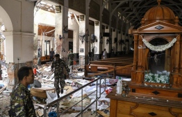 Sri Lankan security personnel walk past dead bodies covered with blankets amid blast debris at St. Anthony's Shrine following an explosion in the church in Kochchikade in Colombo on April 21, 2019.
A string of blasts ripped through high-end hotels and churches holding Easter services in Sri Lanka on April 21, killing at least 156 people, including 35 foreigners. ISHARA S. KODIKARA / AFP
