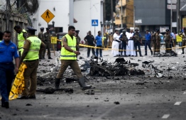 Sri Lankan security personnel inspect the debris of a car after it explodes when police tried to defuse a bomb near St. Anthony's Shrine as priests look on in Colombo on April 22, 2019, a day after the series of bomb blasts targeting churches and luxury hotels in Sri Lanka. - The death toll from bomb blasts that ripped through churches and luxury hotels in Sri Lanka rose dramatically April 22 to 290 -- including dozens of foreigners -- as police announced new arrests over the country's worst attacks for more than a decade. (Photo by Jewel SAMAD / AFP)