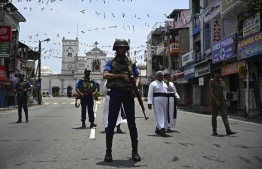 Priests walk on a blocked street as soldiers stand guard outside St. Anthony's Shrine in Colombo on April 25, 2019, following a series of bomb blasts targeting churches and luxury hotels on the Easter Sunday in Sri Lanka. - All of Sri Lanka's Catholic churches have been ordered to stay closed and suspend services until security improves after deadly Easter bombings, which killed at least 359 people and wounded hundreds, a senior priest told AFP on April 25. (Photo by Jewel SAMAD / AFP)