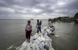 Bangladeshi children walk over the top of a sandbag embankment that was breached by high waters in Khulna on May 4, 2019, as Cyclone Fani reached Bangladesh. - Cyclone Fani, one of the biggest to hit India in years, barrelled into Bangladesh on May 4 after leaving a trail of deadly destruction in India. (Photo by MUNIR UZ ZAMAN / AFP)