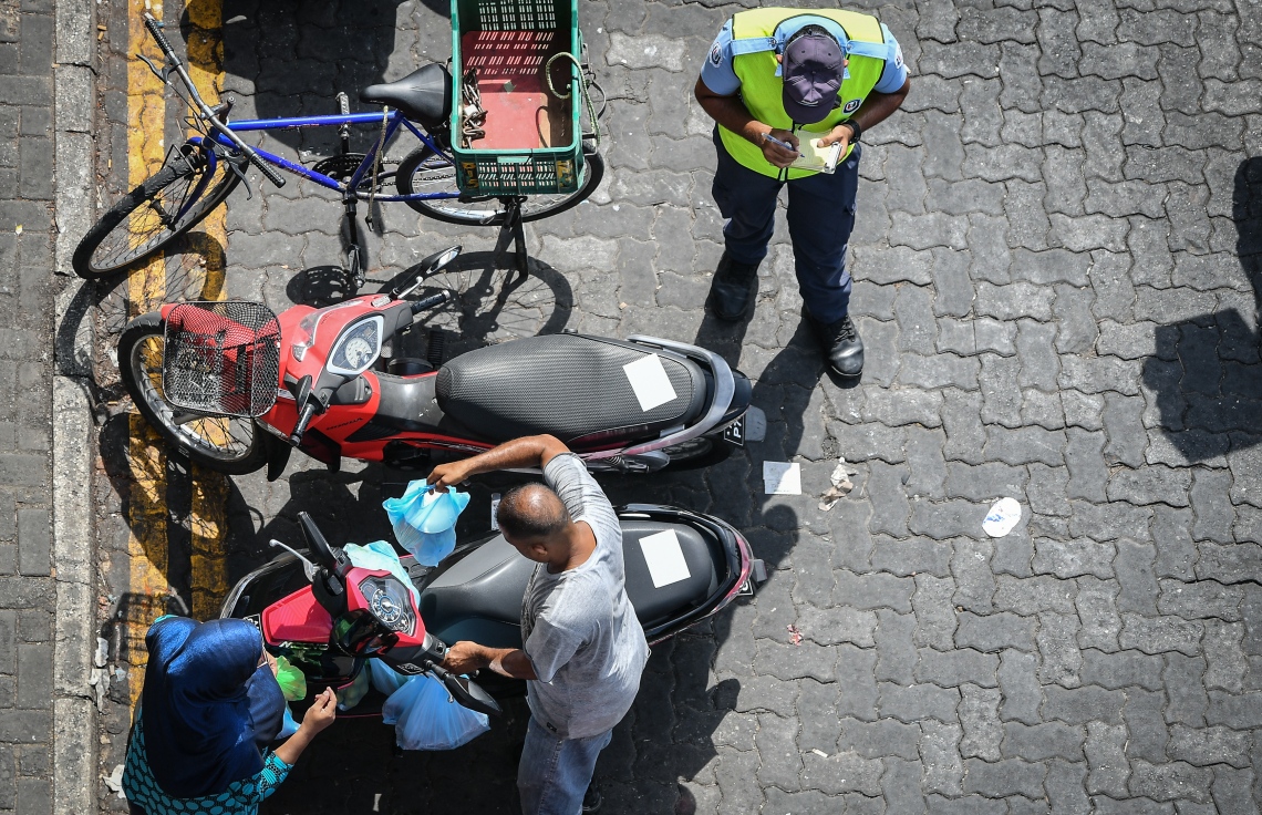 މާލެ: މޭ 5، 2019- މުލަ ރޯދަ އަށް ދެ މީހަކު ބާޒާރުކޮށްގެން ގެންދާ ސާމާނުތަކެއް ސައިކަލްގެ ވަށިގަނޑަށް ލާއިރު، އެ މީހުންގެ ސައިކަލާއި ކައިރީގައި ޕާކް ކޮށްފައި ހުރި އެހެން ސައިކަލެއްގައި ޓްރެފިކް ވަޔަލޭޝަން ސްޓިކާ ޖަހާފައި. އަދި މަސް މާރުކޭޓު ސަރަހައްދުގައި ގަވައިދާ ޚިލާފަށް ޕާކްކުރާ ވެހިކަލްތަކުގައި ސްޓިކާ ޖެހުމުގައި ފުލުހަކު އަވަދިނެތި ހަރަކާތްތެރިވަނީ.---ފޮޓޯ: ނިޝާން އަލީ/މިހާރު