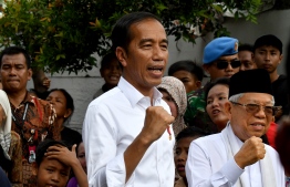 Indonesian President Joko Widodo (C) and his running mate Ma'ruf Amin (R) gesture while visiting a neighbourhood in Jakarta on May 21, 2019. - Thousands of soldiers fanned out across Jakarta on May 21 after the surprise early announcement of official results in Indonesia's election showed Joko Widodo re-elected leader of the world's third-biggest democracy. (Photo by GOH Chai Hin / AFP)