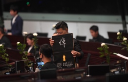 Pro-democracy lawmaker Gary Fan (C) holds a placard as he and other pro-democracy lawmakers hold five minutes of silence in the Legislative Council in Hong Kong on June 19, 2019, for a man who fell to his death on June 15 during a protest against a controversial extradition bill. - Massive rallies over the past two weeks against a Beijing-backed proposed law that would have allowed extraditions to mainland China have drawn support from a wide political and social spectrum, from students and activists to social workers and the business community, and -- based on figures from organisers -- were the biggest in Hong Kong's history. (Photo by Anthony WALLACE / AFP)