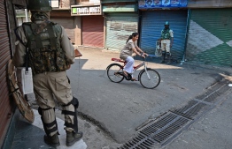 Indian paramilitary troopers stand guard as a Kashmiri girl rides a bicycle after authorities imposed restrictions on movement in Srinagar on July 8, 2019. - Indian authorities imposed restrictions of movement around the Jamia Masjid mosque in Srinagar on July 8 during a one-day strike called by Kashmiri seperatists on the third anniversary of the death of militant commander Burhan Wani. (Photo by STR / AFP)