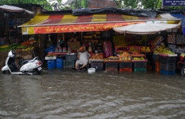 A vendor sits under cover at his flooded fruit shop during heavy monsoon rain in Amritsar on July 20, 2019. (Photo by NARINDER NANU / AFP)