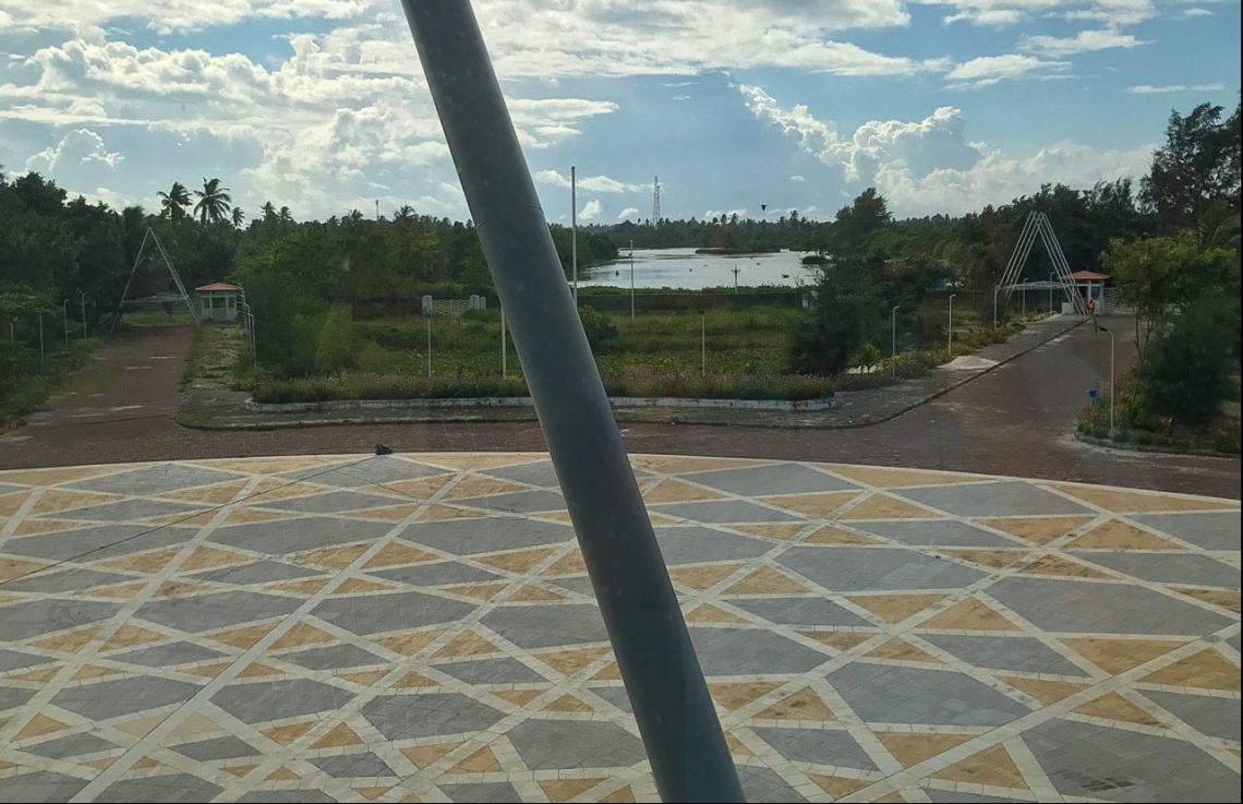 އައްޑޫ އާ ހޮސްޕިޓަލްގެ އެތެރޭގެ ކޮޓަރިއަކުން، އެ ހޮސްޕިޓަލްގެ މައި ގޭޓު ސަރަހައްދު ފެންނަ ގޮތް: މި އިމާރާތުގެ ވަށައިގެންވާ ސަރަހައްދުގެ ލޭންޑް ސްކޭޕިން އަށް ފަހުން ބަދަލުތަކެއް ގެންނާނެ.---ފޮޓޯ: މިހާރު