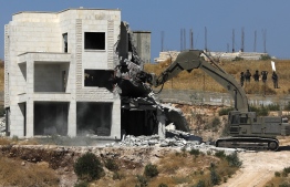 This picture taken from Jerusalem on July 22, 2019 shows Israeli security forces tearing down one of the Palestinian buildings still under construction which have been issued notices to be demolished in the West Bank village of Dar Salah, adjacent to the Sur Baher area which straddles the West Bank and Jerusalem. - Palestinians accuse Israel of using security as a pretext to force them out of the area, meant to be under Palestinian Authority civilian control under the Oslo accords, as part of long-term efforts to expand settlements and roads linked them. An Israeli high court ruling in June 2019 dismissed a petition by Palestinian residents requesting the cancellation of a military order prohibiting construction, and residents received a 30-day notice from Israeli authorities informing them of their intent to demolish the homes. (Photo by Ahmad GHARABLI / AFP)