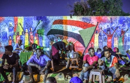 (FILES) In this file photo taken on April 24, 2019, Sudanese protesters sit in front of a recently painted mural during a demonstration near the army headquarters in the capital Khartoum. - The graffiti that symbolised Sudan's uprising are being painted over across the capital Khartoum, protest leaders complained Wednesday, urging the military authorities to stop their whitewashing. The Forces for Freedom and Change that led the months-long protest movement that brought down longtime ruler Omar al-Bashir said the "enemies of the revolution" had been systematically erasing murals. (Photo by OZAN KOSE / AFP)